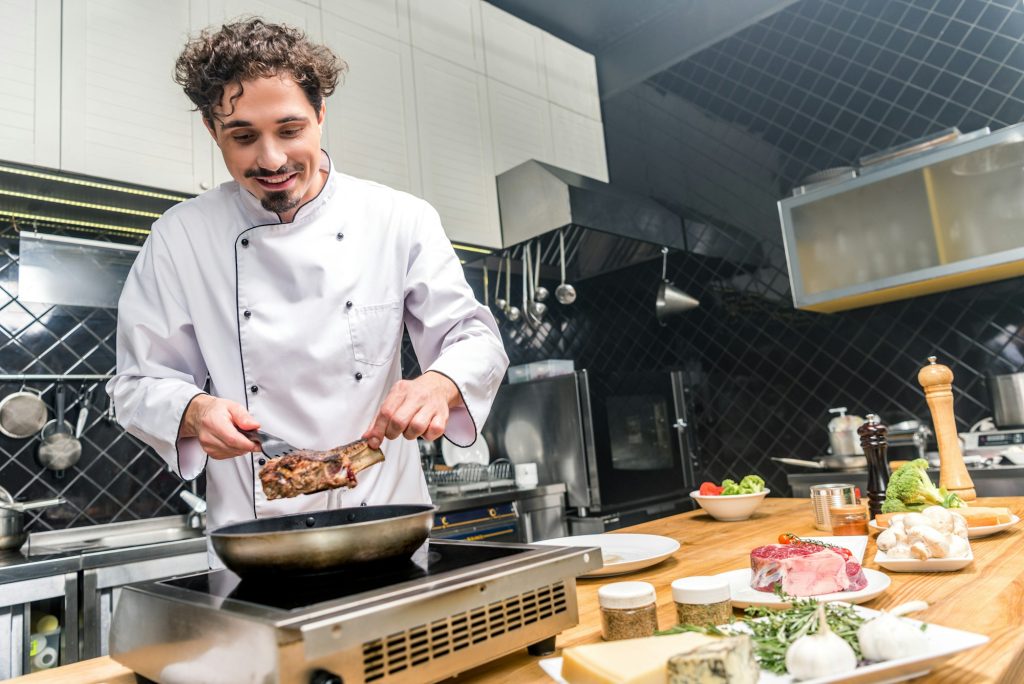 smiling chef frying meat in restaurant kitchen